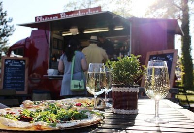 Foodtruck mit interessierten Menschen im Hintergrund des Bildes, sowie einen Flammkuchen im Fokus des Bildes